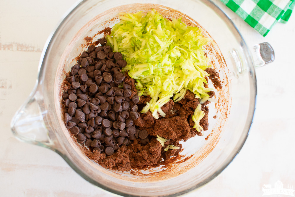 a mixing bowl with chocolate cookie dough, grated zucchini, and chocolate chips