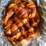 chicken legs in a slow cooker lined with a plastic bag. Chicken is coated with rub and drizzled with bbq sauce