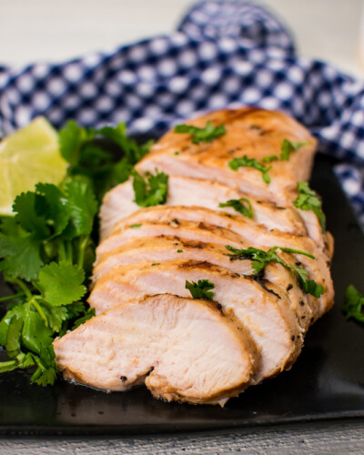 Sliced grilled chicken showing how juicy it is, garnished with cilantro on a black plate