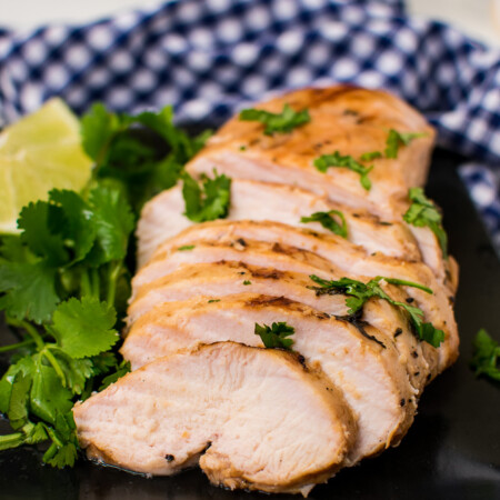 Sliced grilled chicken showing how juicy it is, garnished with cilantro on a black plate