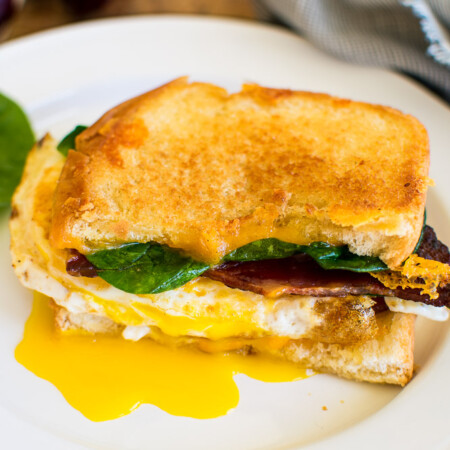 Half a fried egg grilled cheese sandwich with spinach and bacon. Red grapes in the background.