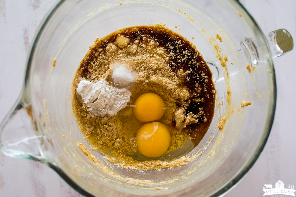 a glass mixing bowl with two eggs, baking powder, vanilla, and creamed butter and brown sugar