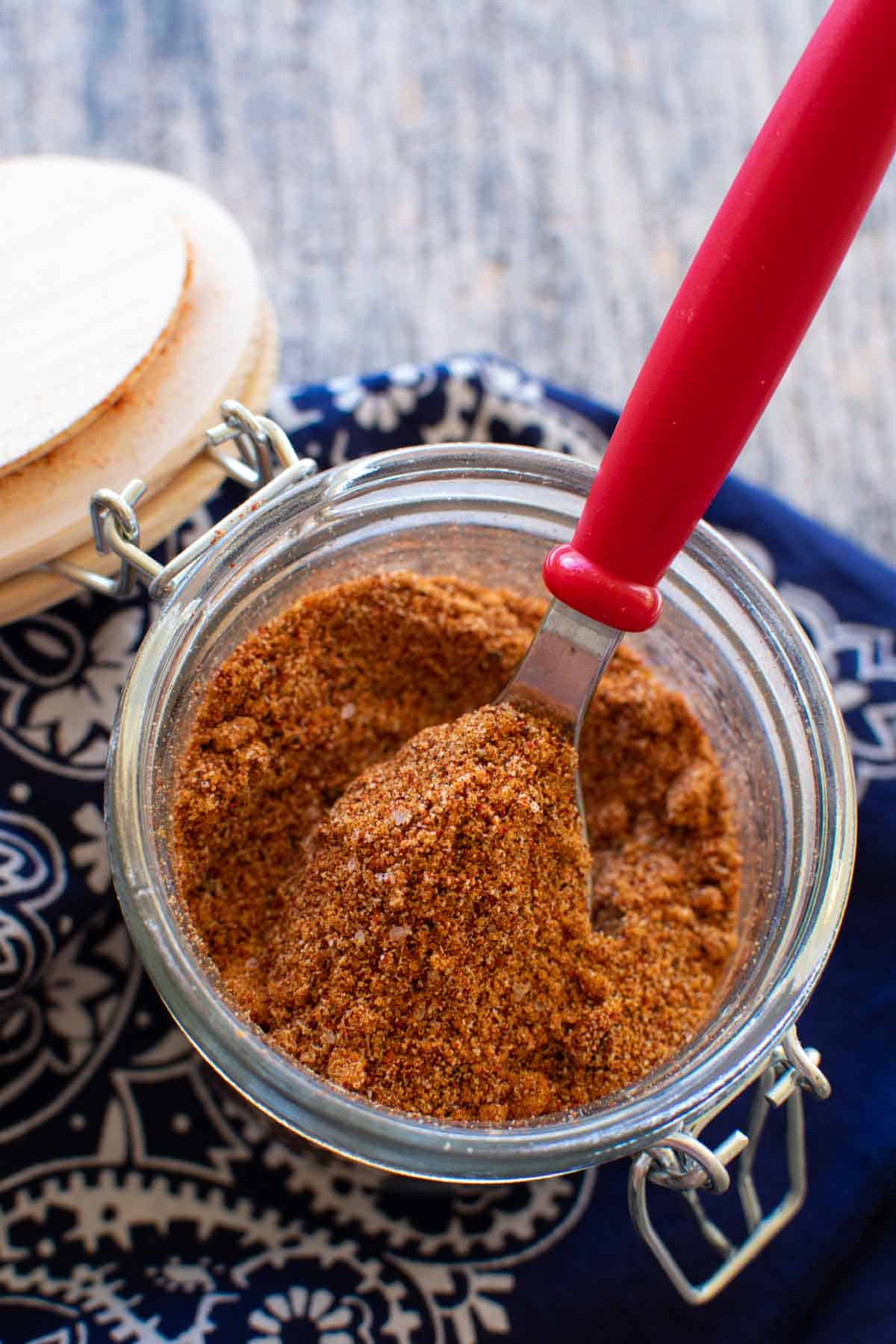 A jar of chicken rub with a red spoon in it.