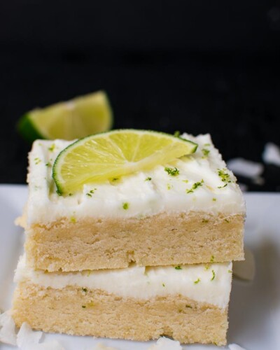 two sugar cookie bars stacked on top of each other with white frosting and a lime wedge