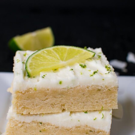 two sugar cookie bars stacked on top of each other with white frosting and a lime wedge