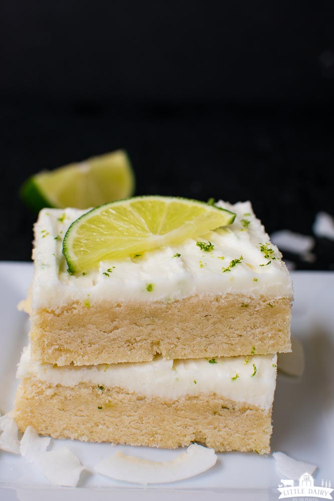 two coconut lime sugar cookie bars stacked on top of each other with white frosting and a lime wedge