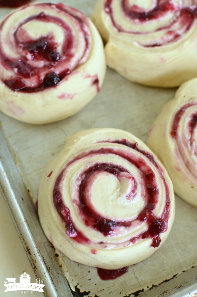 a sheet pan with raw cinnamon rolls filled with blueberry sauce