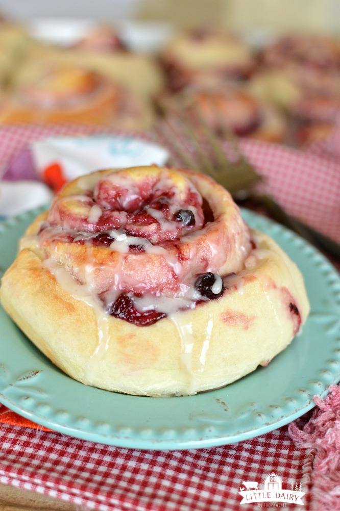 a light blue plate with a sweet roll filled with blueberry filling and topped with icing on a red and white napkin