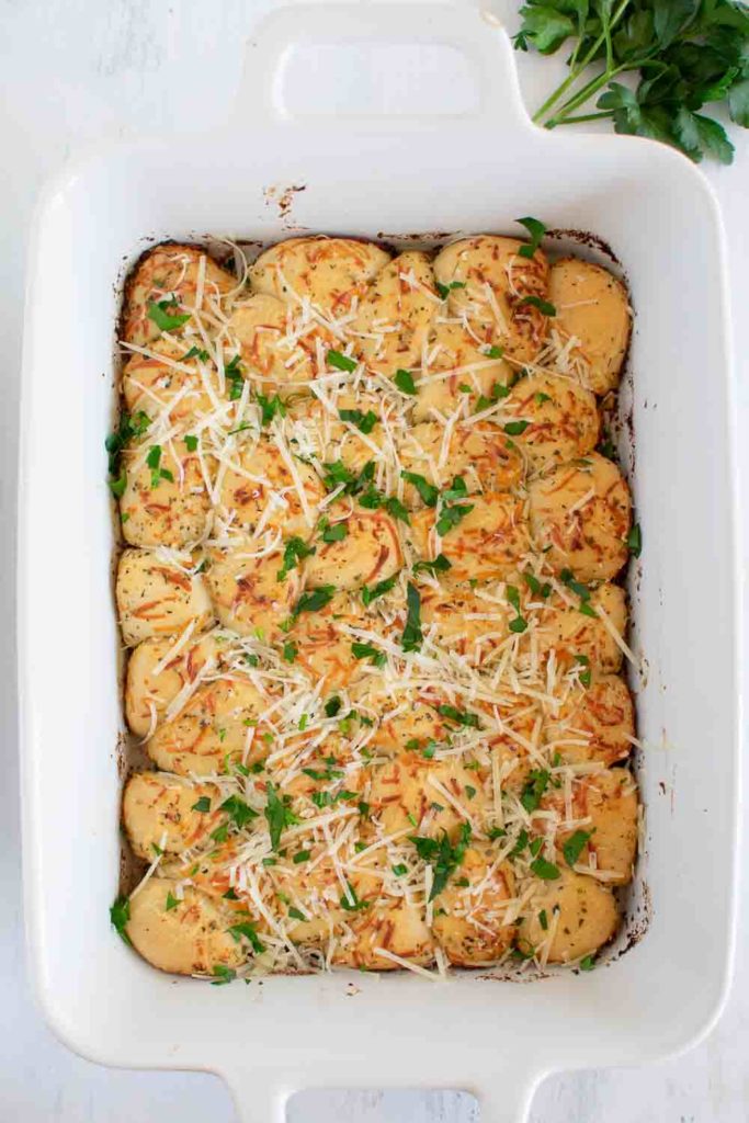 a baking pan with baked pull apart dinner rolls sprinkled with cheese and herbs