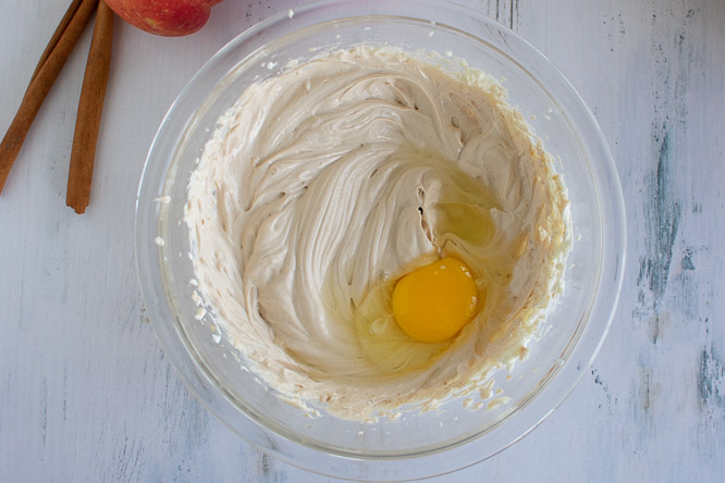 a glass bowl with beaten cream cheese mixture and a raw egg