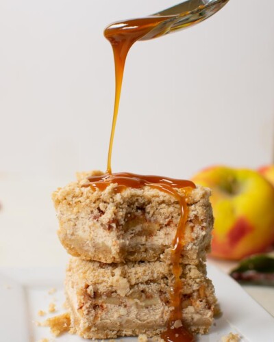 two cheesecake bars stacked on top of each other and a spoon drizzling caramel over the top