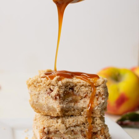 two cheesecake bars stacked on top of each other and a spoon drizzling caramel over the top