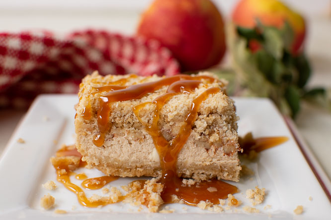 a cheesecake bar with cinnamon apples, a crumb crust, and drizzled with caramel