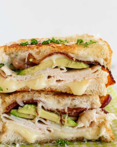 a hot turkey sandwich cut in half and topped with avocado, turkey, and bacon