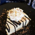 Top view of a piece of banana cream pie with chocolate drizzle on a black plate