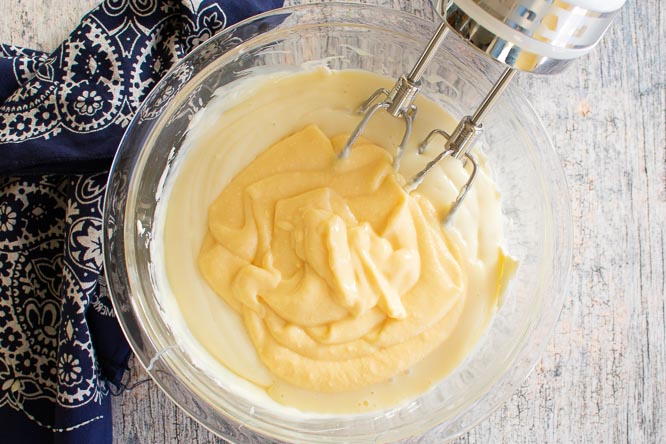 A mixing bowl with instant pudding and custard being mixed by a handheld mixer