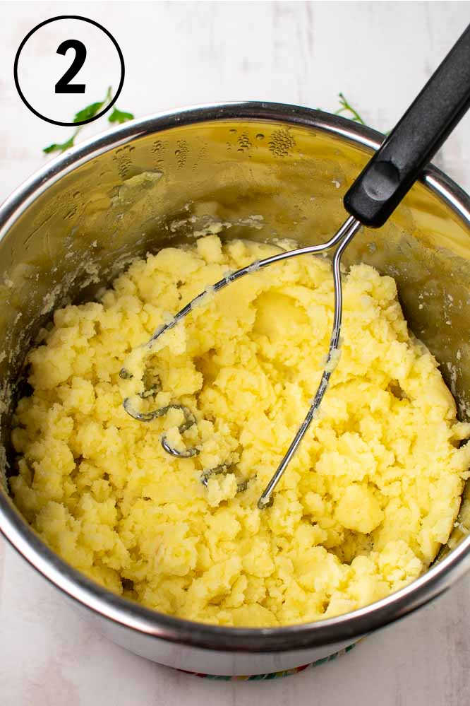 mashed potatoes in a metal pressure cooker pot, with a potato masher