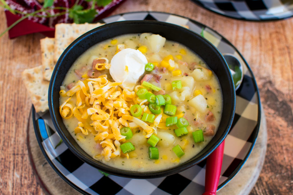 A bowl of ham and potato soup with onions, sour cream, and cheese.