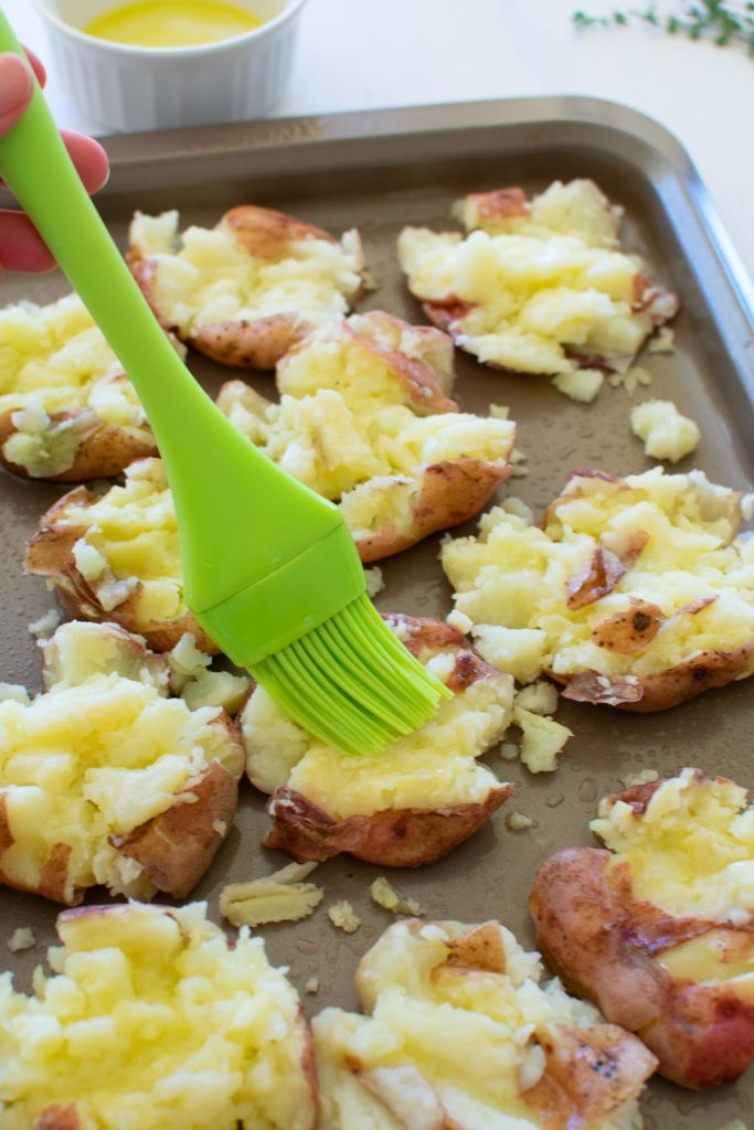 Smashed red potatoes being brushed with melted butter.