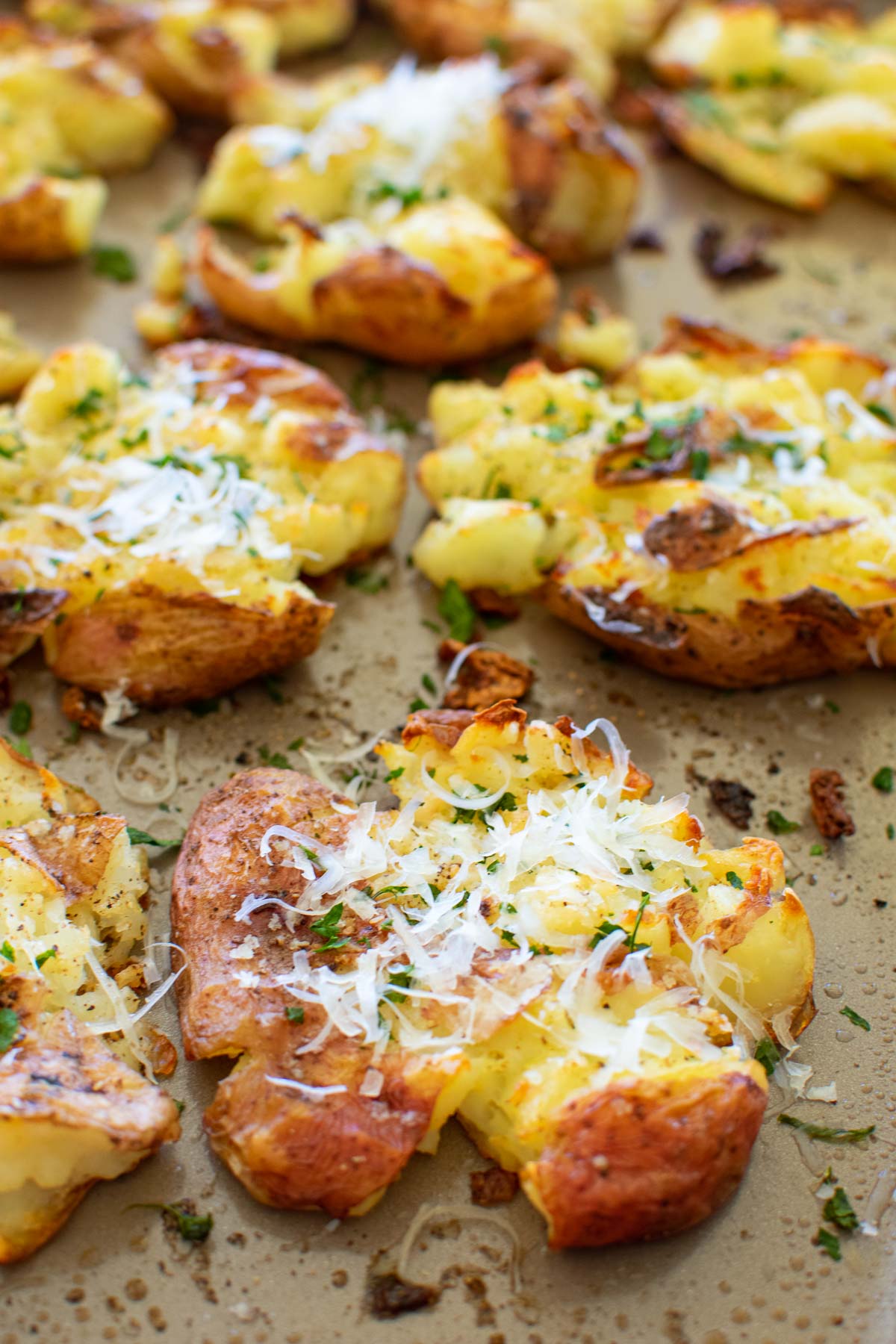 A sheet pan with smashed and baked red potatoes topped with cheese and herbs.
