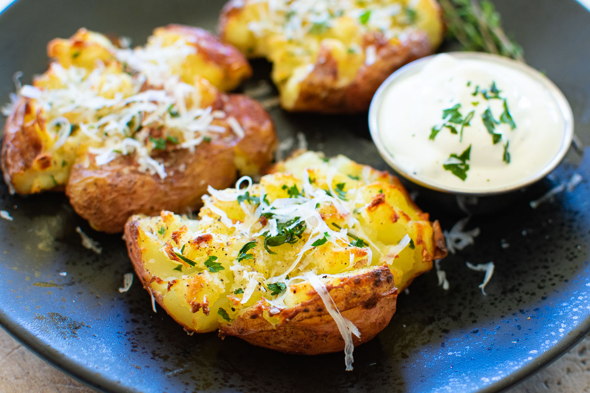 Crispy crushed potatoes on a black plate with ranch dressing.