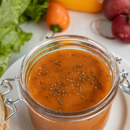 A jar of French dressing with green salad ingredients.