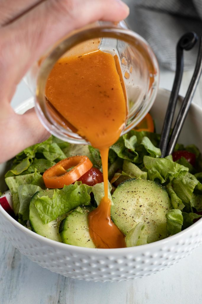 Homemade French dressing being poured over a green salad.