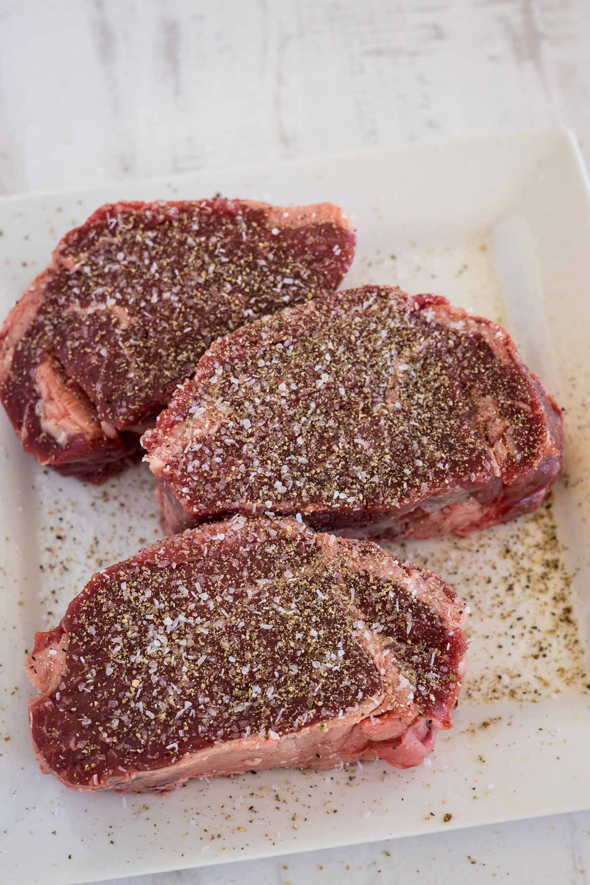 Raw tenderloin steaks seasoned with salt and pepper.