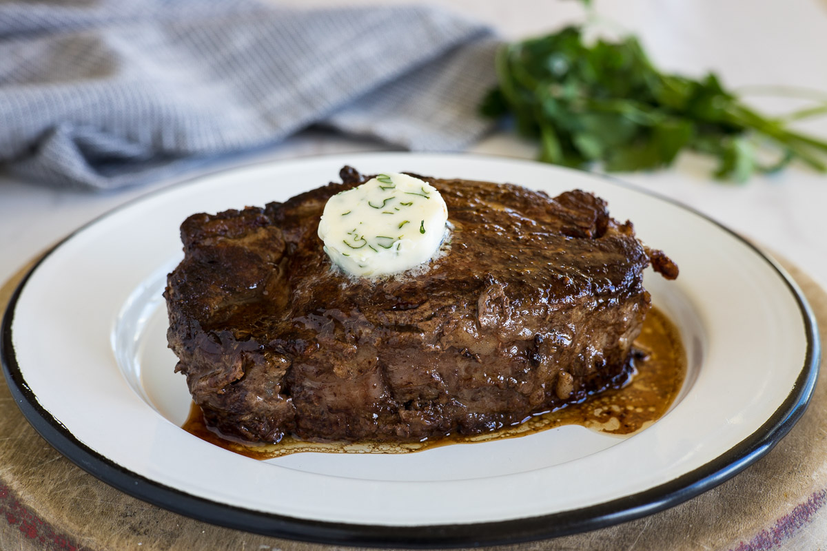 A skillet cooked beef tenderloin steak with butter and herbs on top.