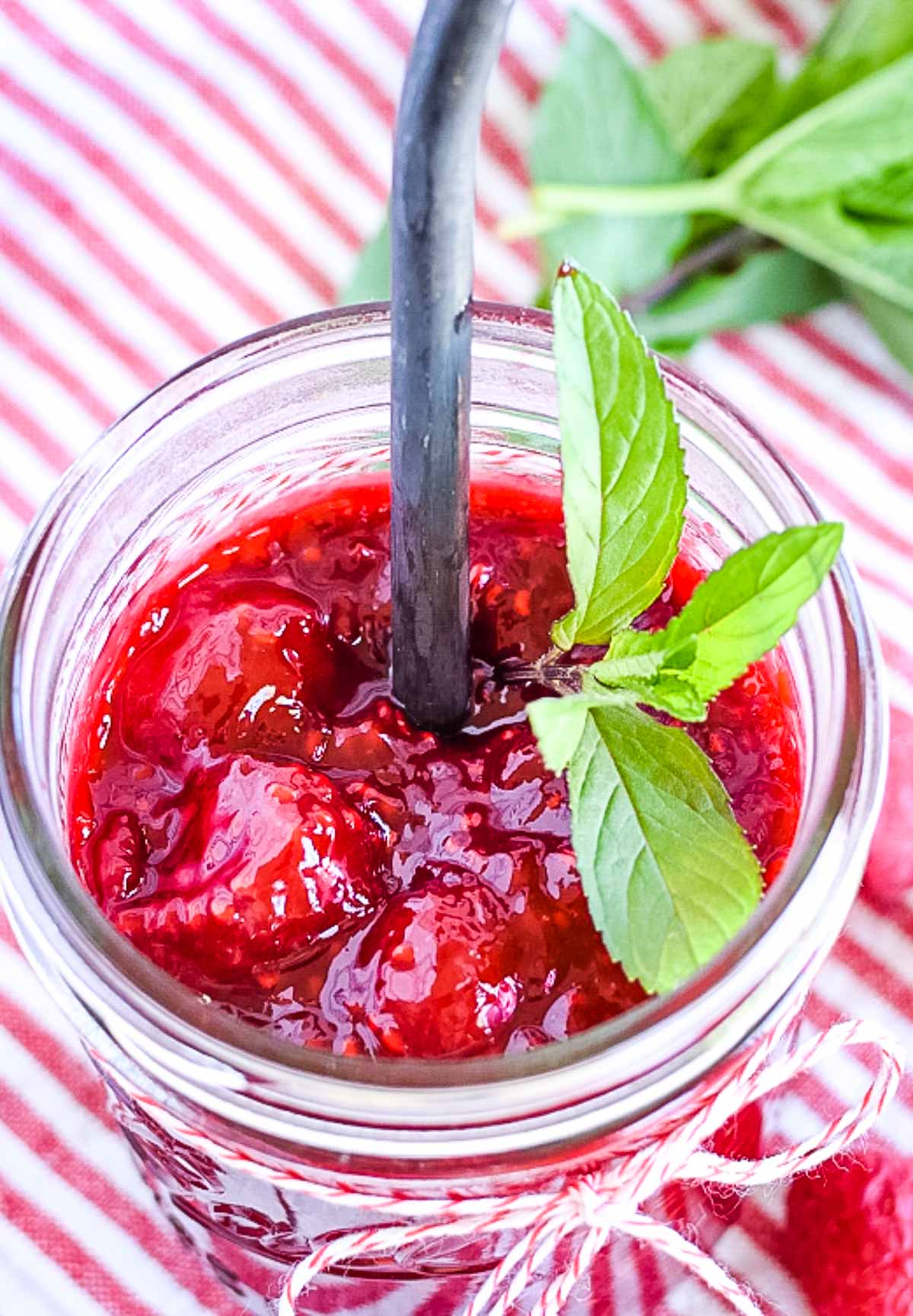 A jar of raspberry topping with a mint leaf.