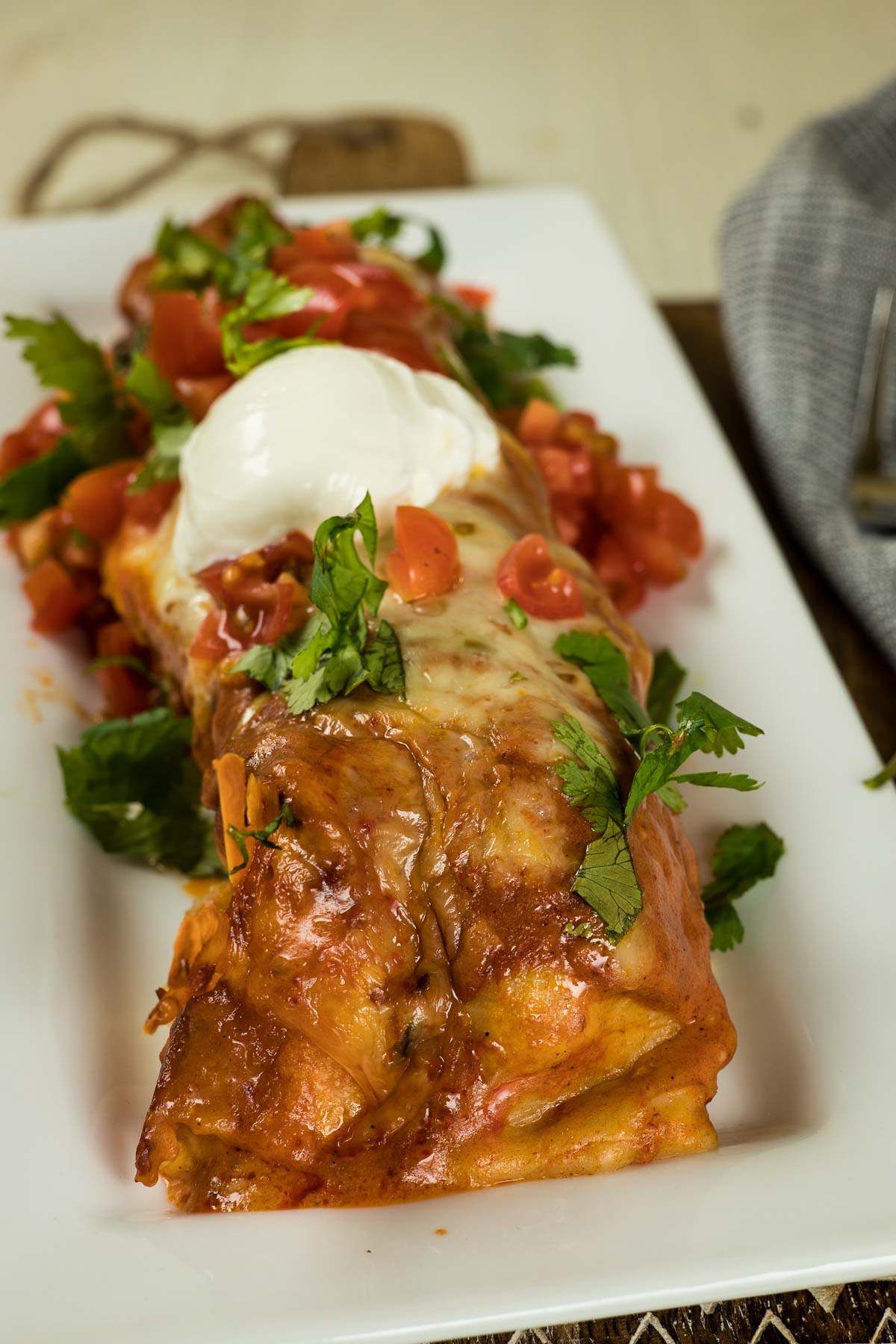 Beef enchilada with sour cream, tomatoes, and cilatnro.