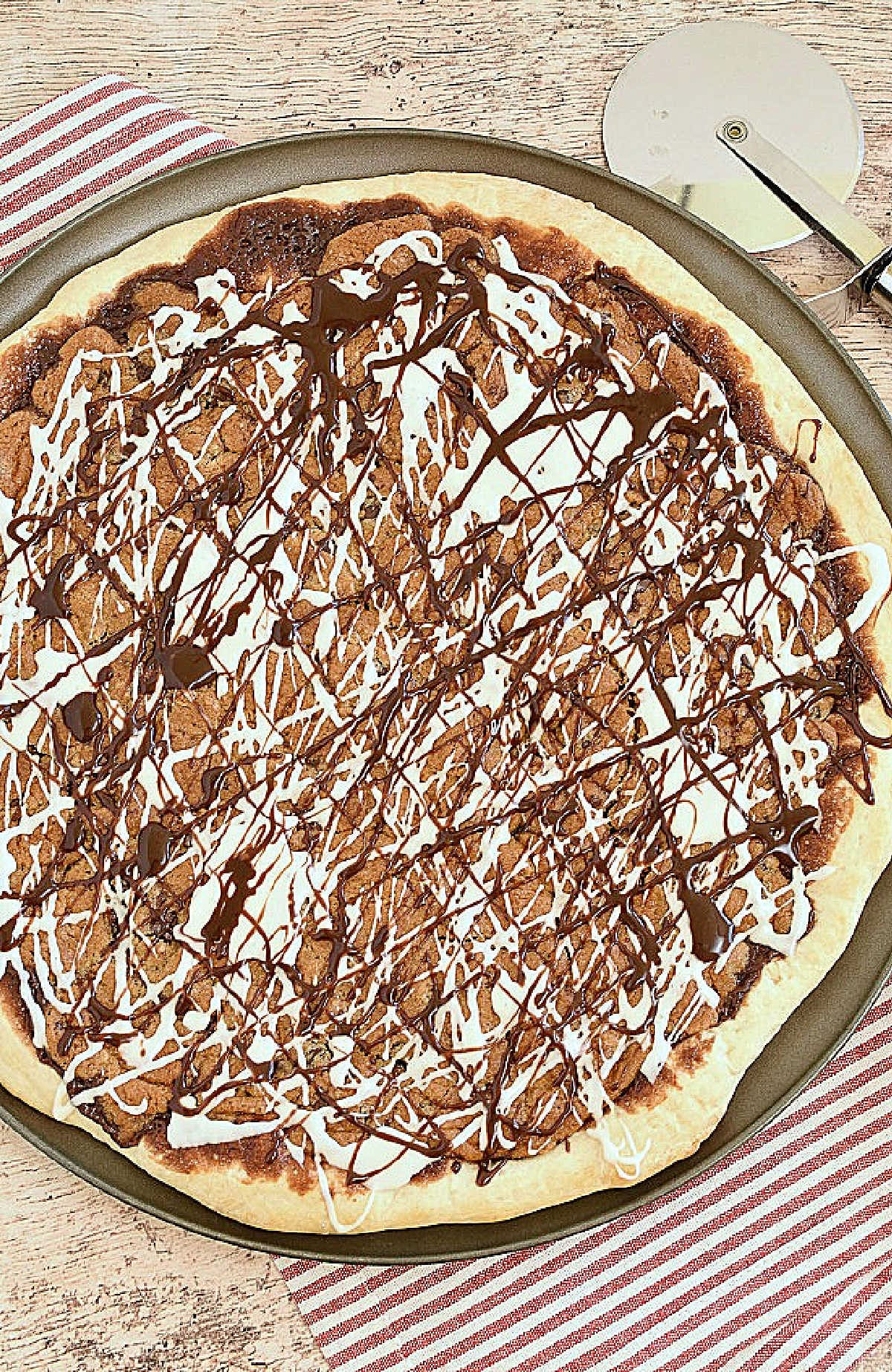 A dessert pizza with baked cookies and vanilla icing drizzled over the top.