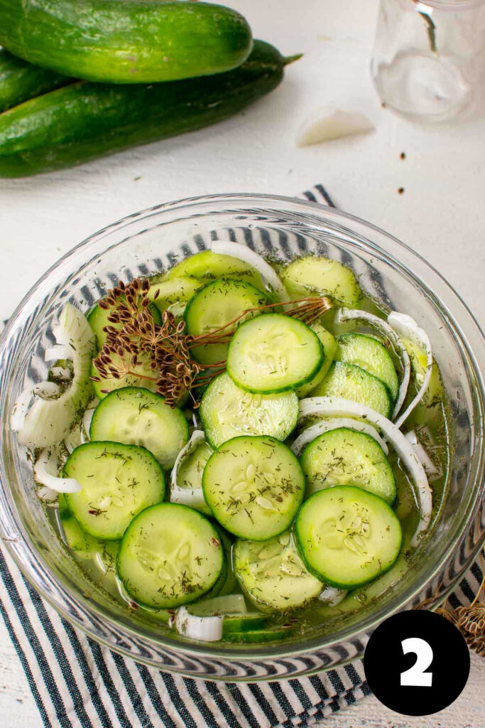 A glass bowl with sliced cucumbers in vinegar with onions and dill.