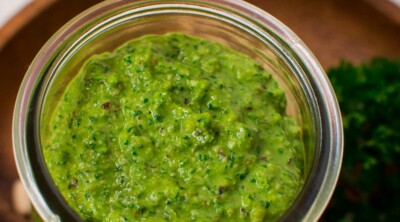 A glass jar with green pesto on a wooden plate.