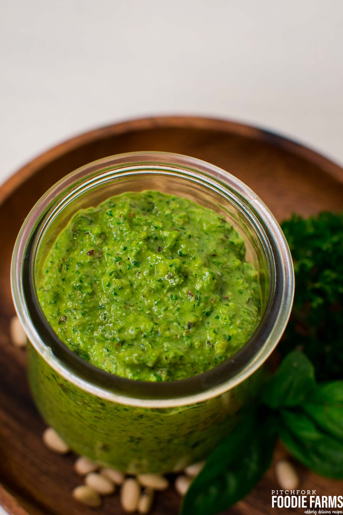 A glass jar with green pesto on a wooden plate.