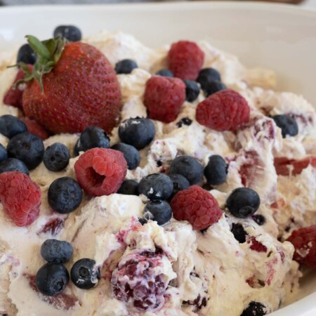 A creamy salad with blueberries, strawberries, and raspberries on top.