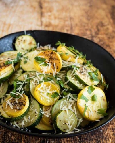 BBQ zucchini in a black bowl with parmesan and fresh parsley.