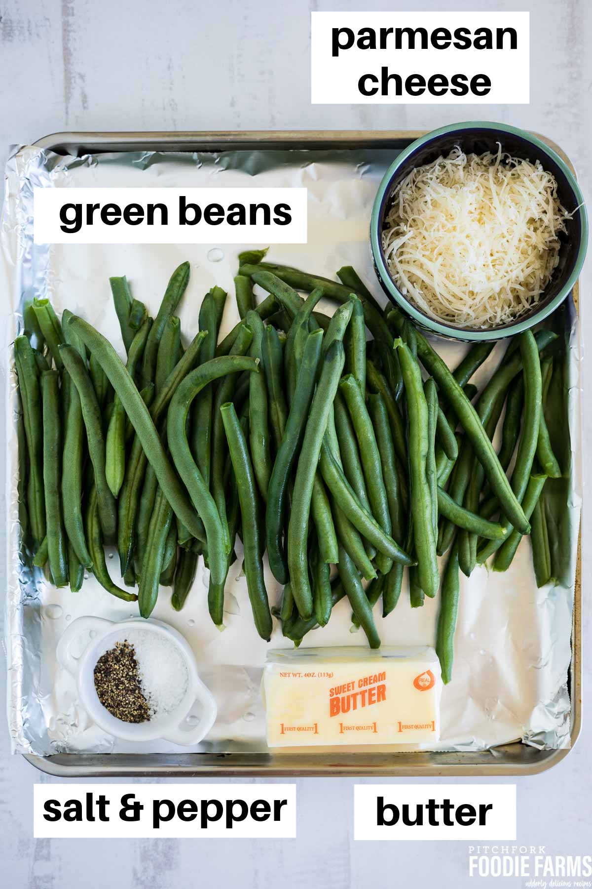 A sheet pan with fresh green beans, a cube of butter, salt and pepper, and grated parmesan cheese.