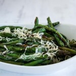 A white dish with green beans topped with shredded parmesan cheese.