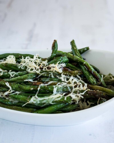 A white dish with green beans topped with shredded parmesan cheese.
