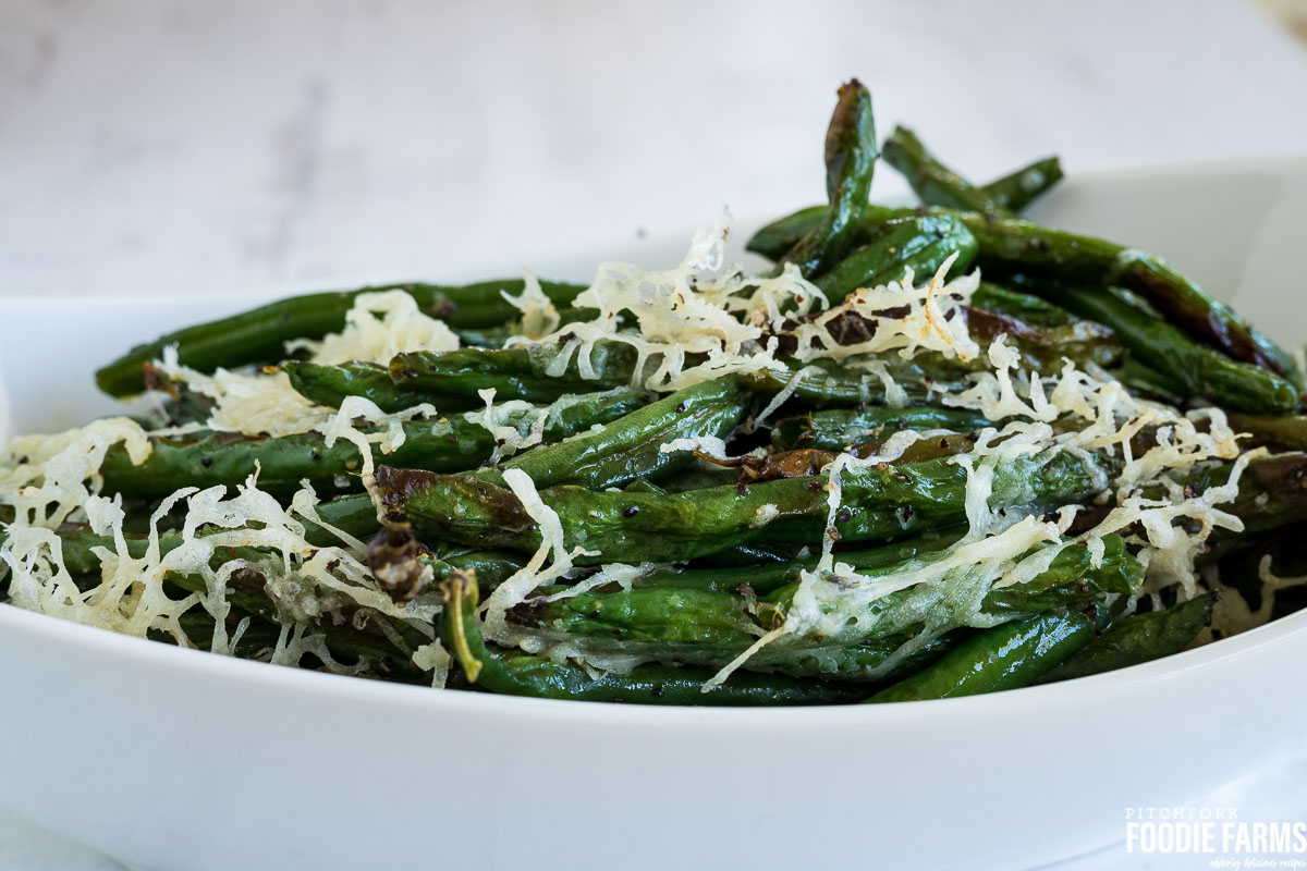 Cooked green beans in a white baking dish topped with grated cheese.