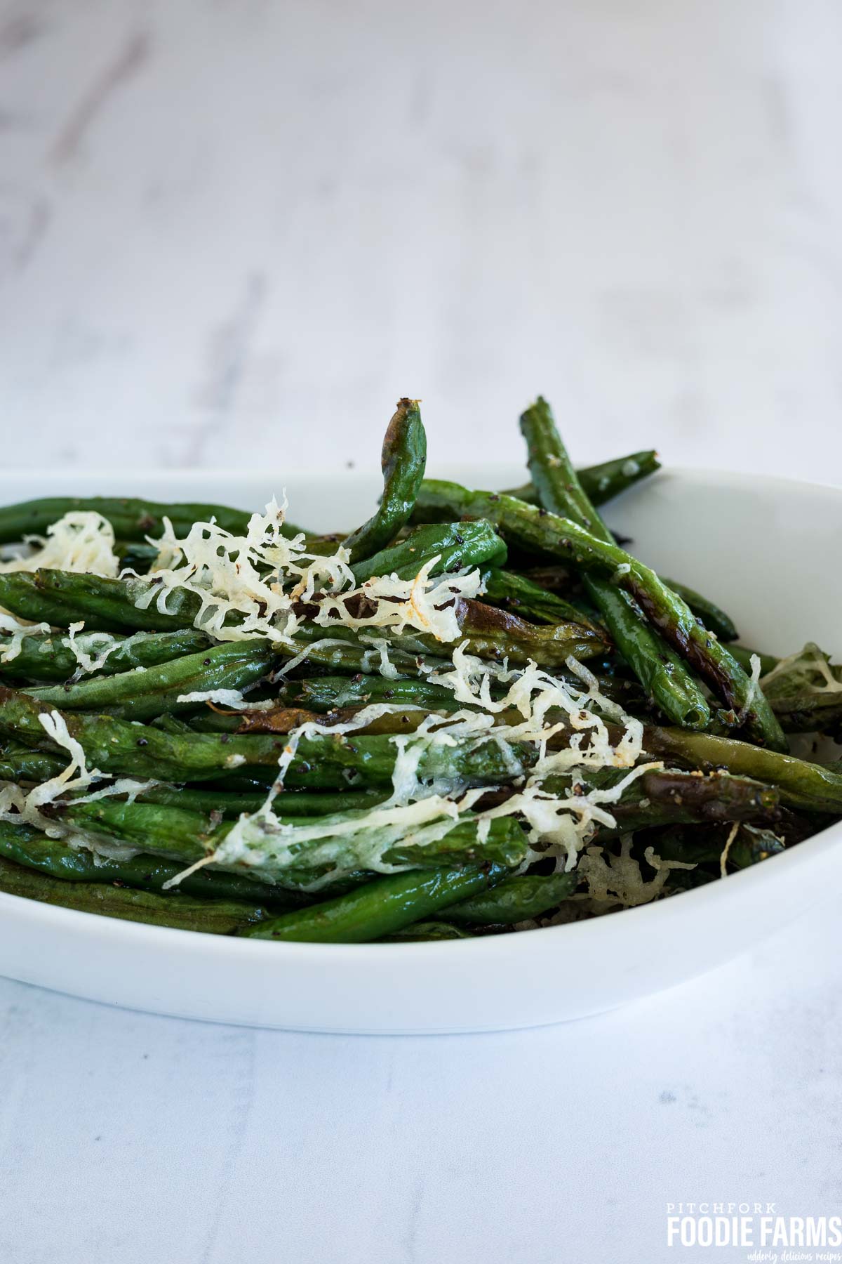 A white dish with green beans topped with shredded parmesan cheese.