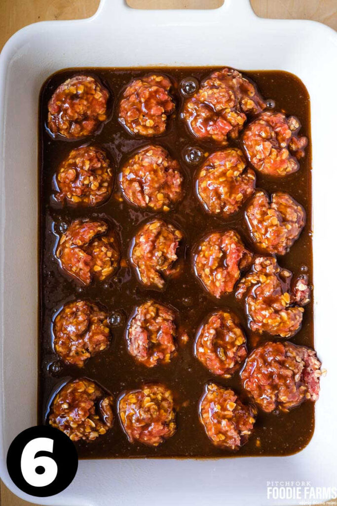 A baking dish with raw meatballs covered in sauce.