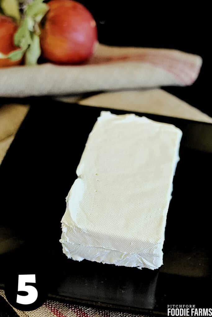 A brick of cream cheese on a black plate.