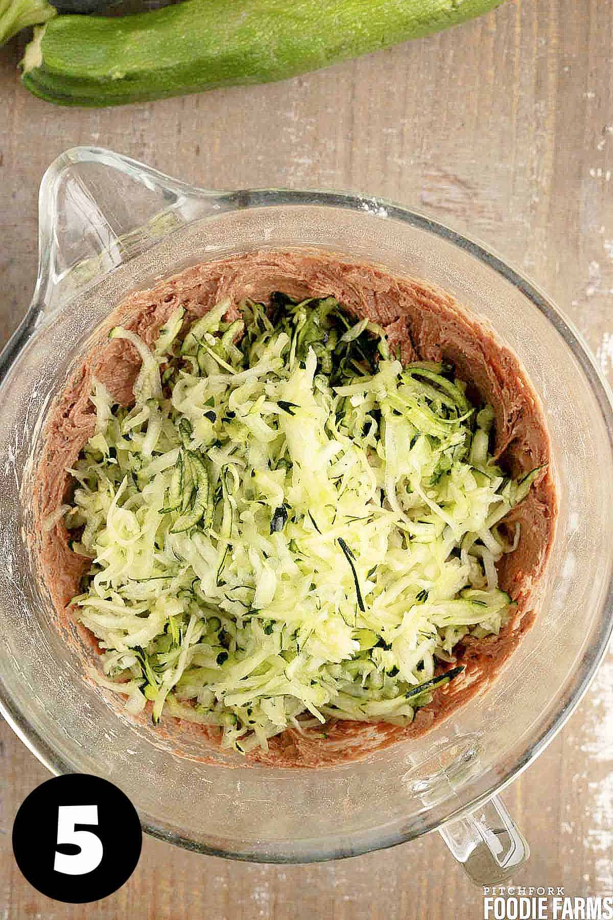 Chocolate cake batter with grated zucchini in a glass mixing bowl.