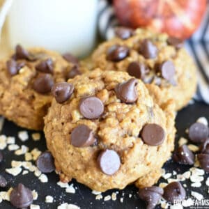 Pumpkin Oatmeal Chocolate Chip Cookies on a black napkin with oats and chocolate chips scattered around.