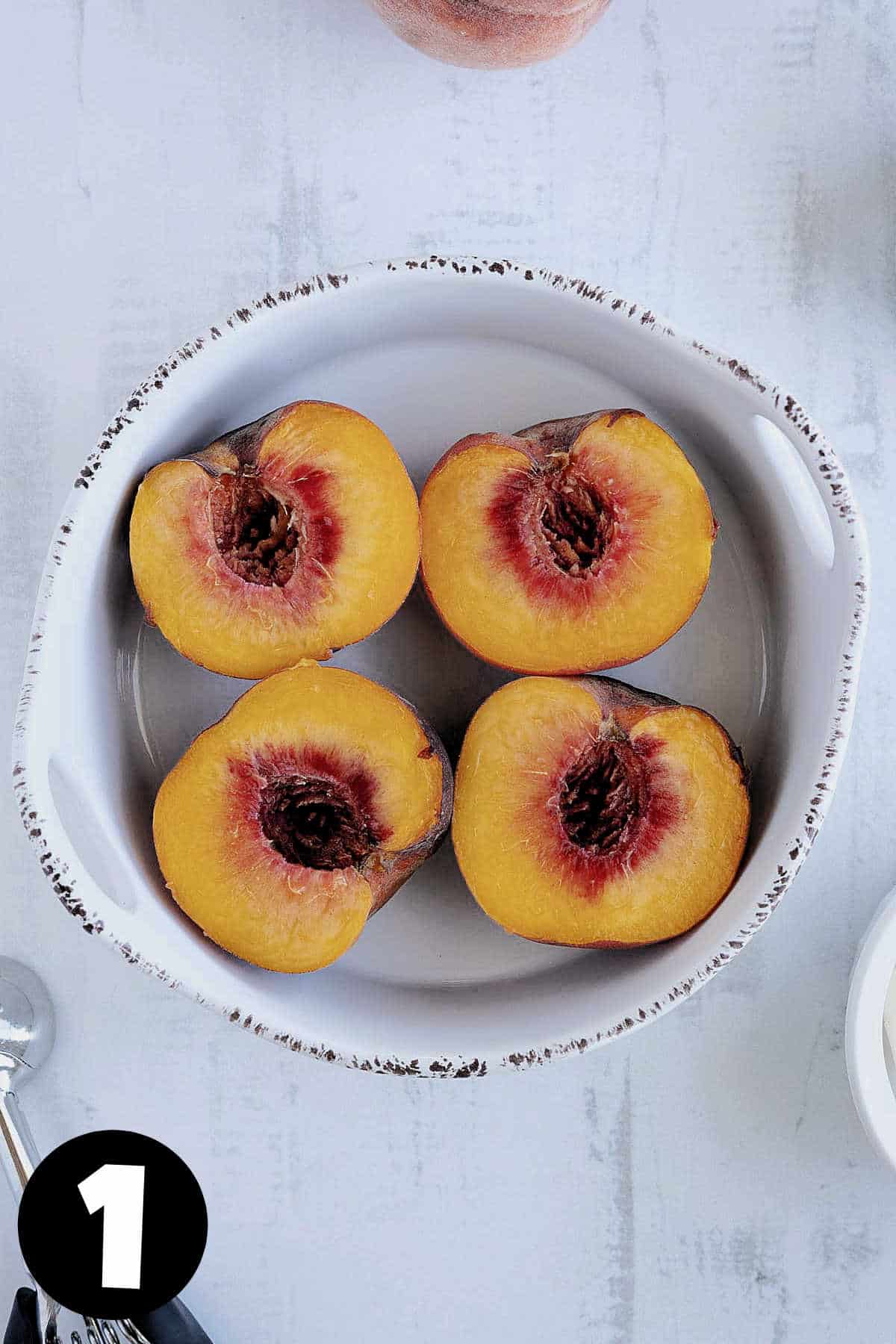Peaches cut in half in a baking dish.