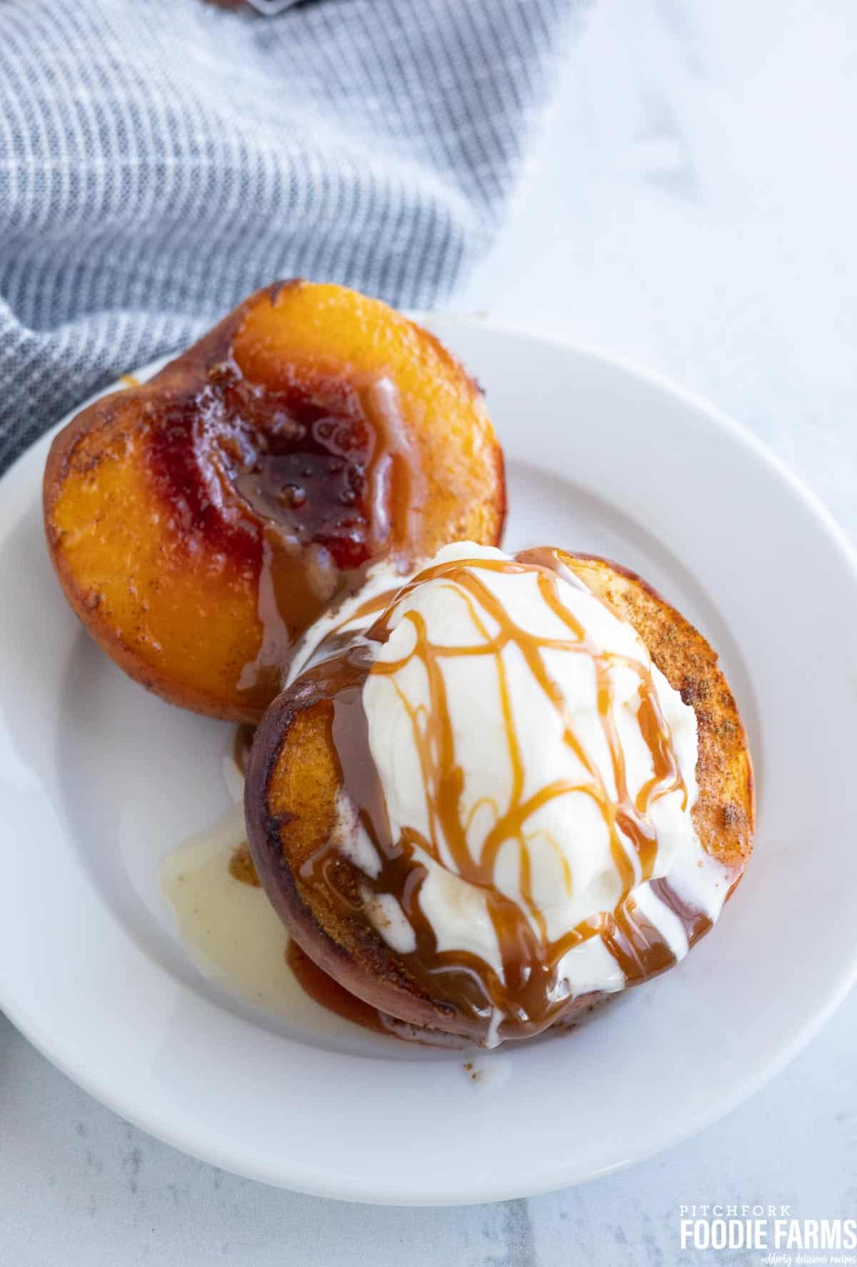 Two baked peach halves topped with vanilla ice cream and drizzled with caramel sauce.
