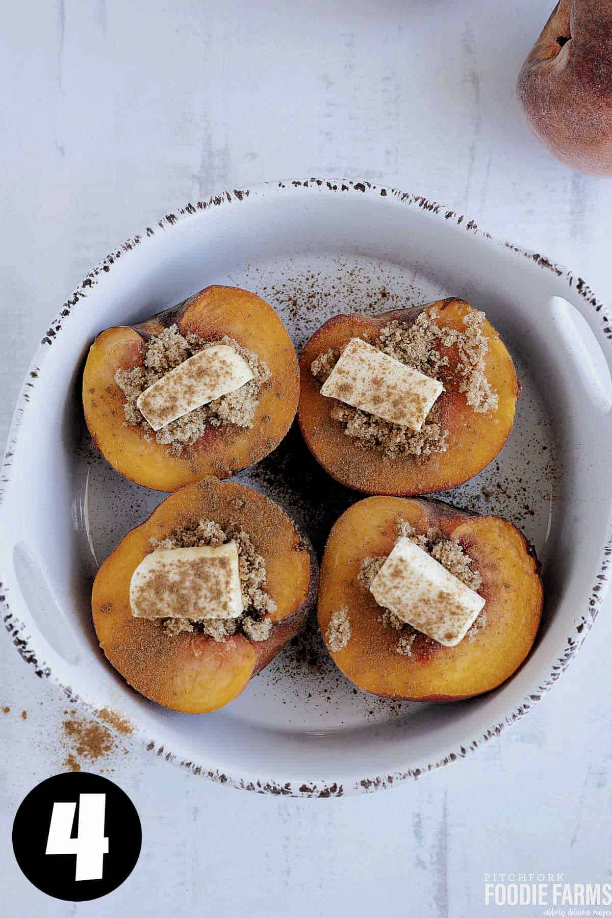Peaches cut in half with butter, brown sugar, and cinnamon in an oven proof dish.