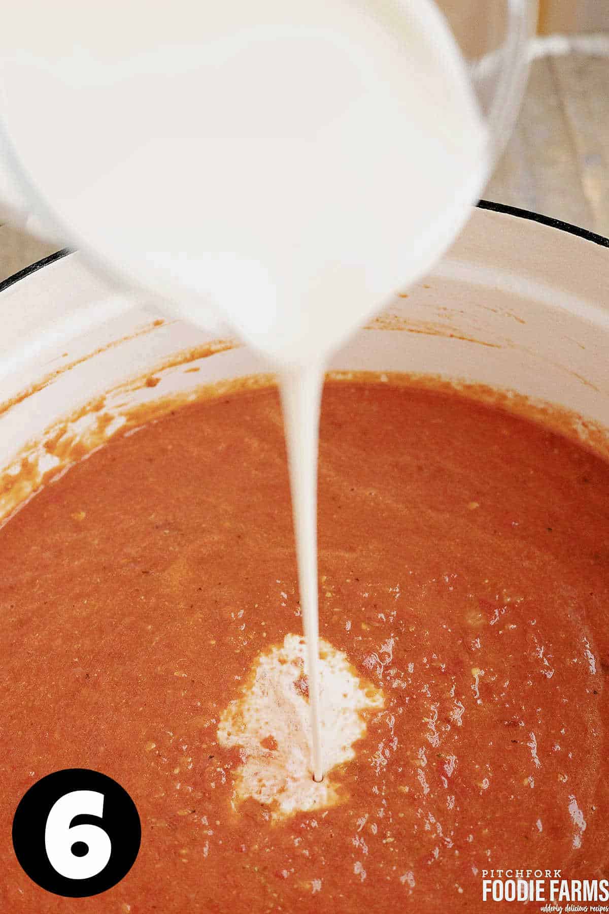 Cream being poured into a pot of creamy tomato soup.